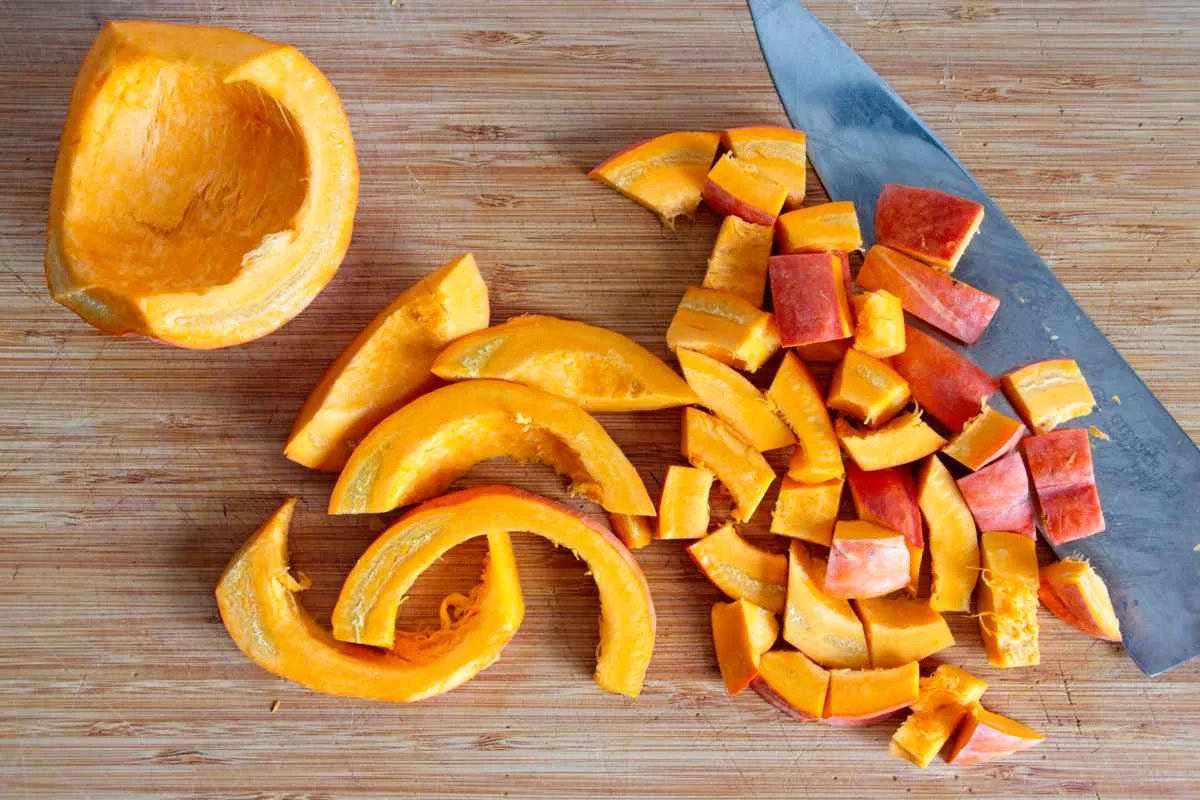 Fresh pumpkin being sliced and chopped on a wooden board with a kitchen knife.