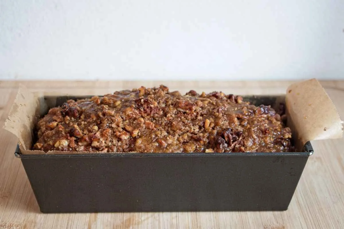 The loaf freshly baked in the tin with the walnut crumble topping set and golden.
