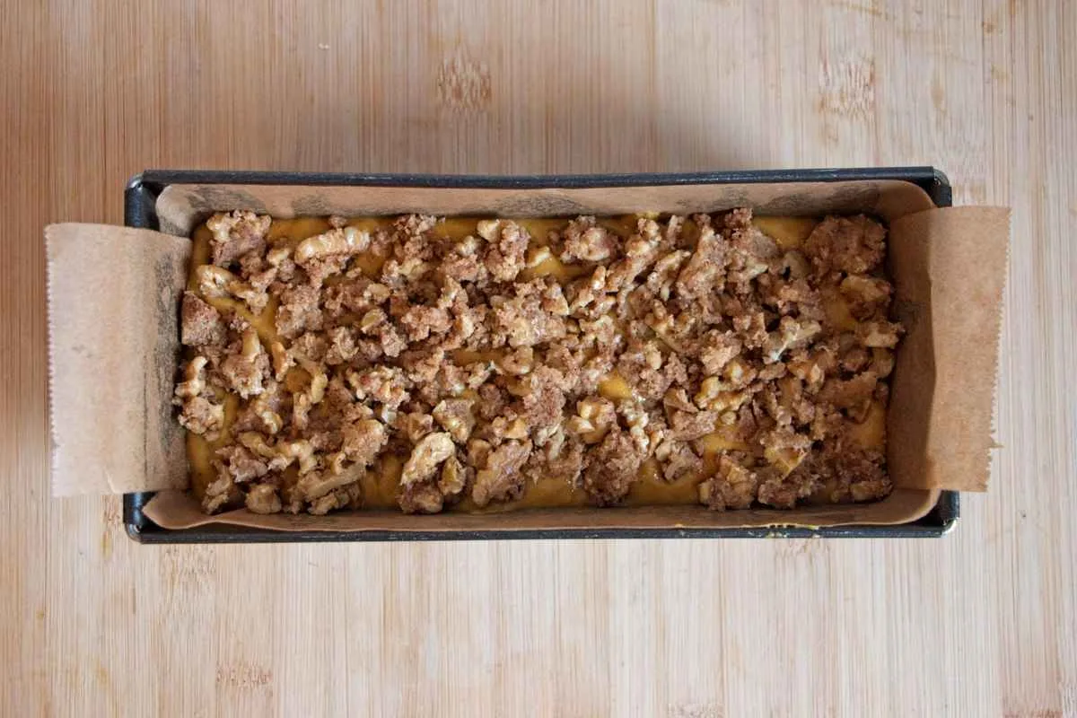 Loaf batter in a lined tin topped with walnut crumble before baking.
