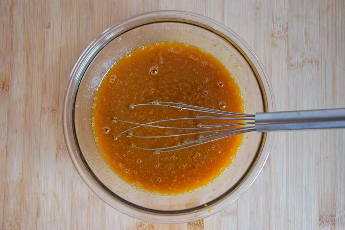 A bowl of mixed wet ingredients with a whisk on a wooden surface.