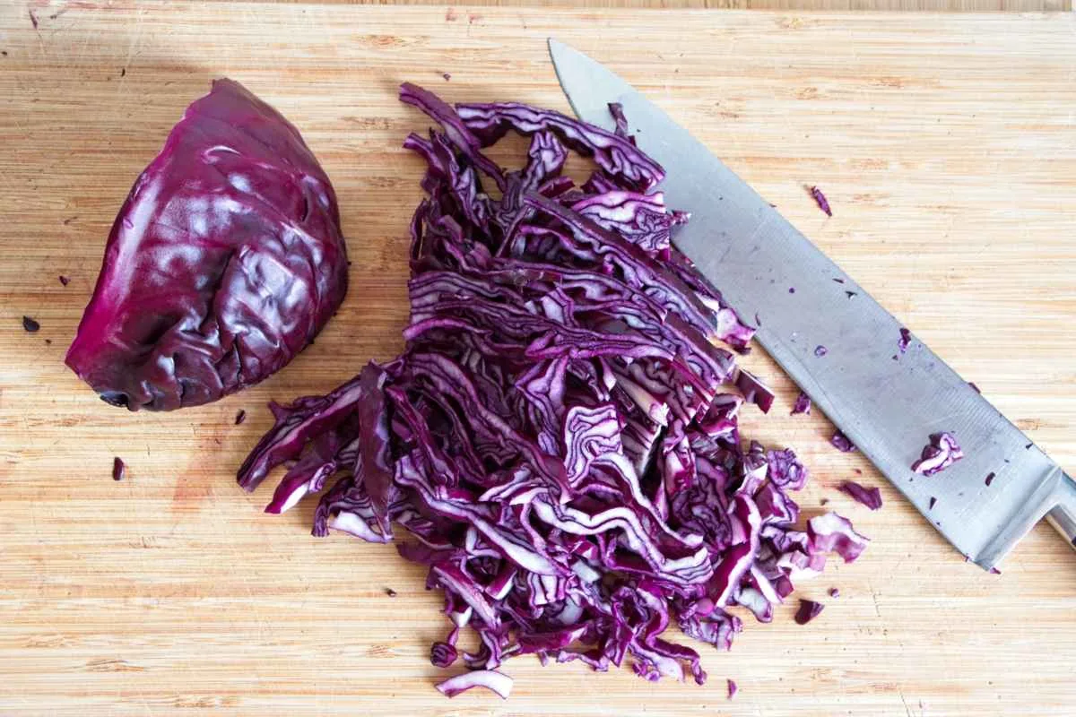 Sliced red cabbage on a wooden board with a chef’s knife beside it.