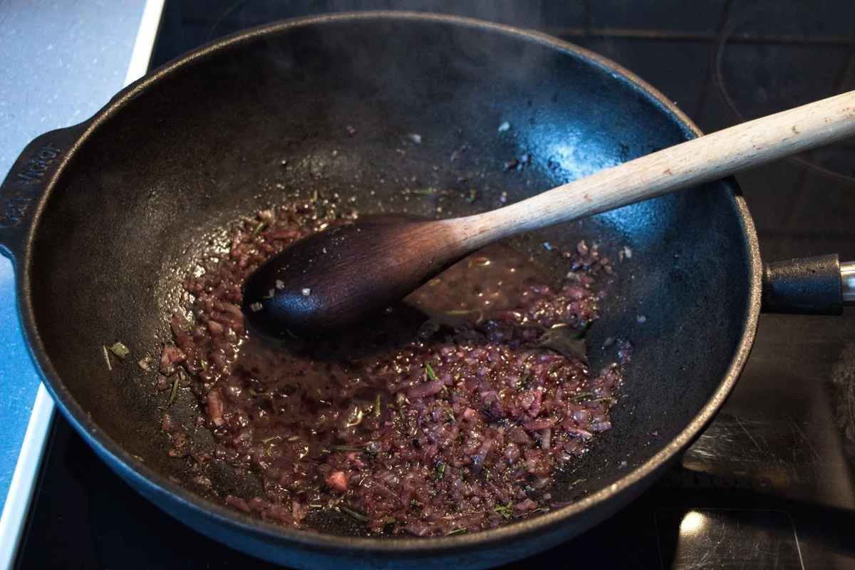 Red wine simmering with softened onions and herbs in a pan.