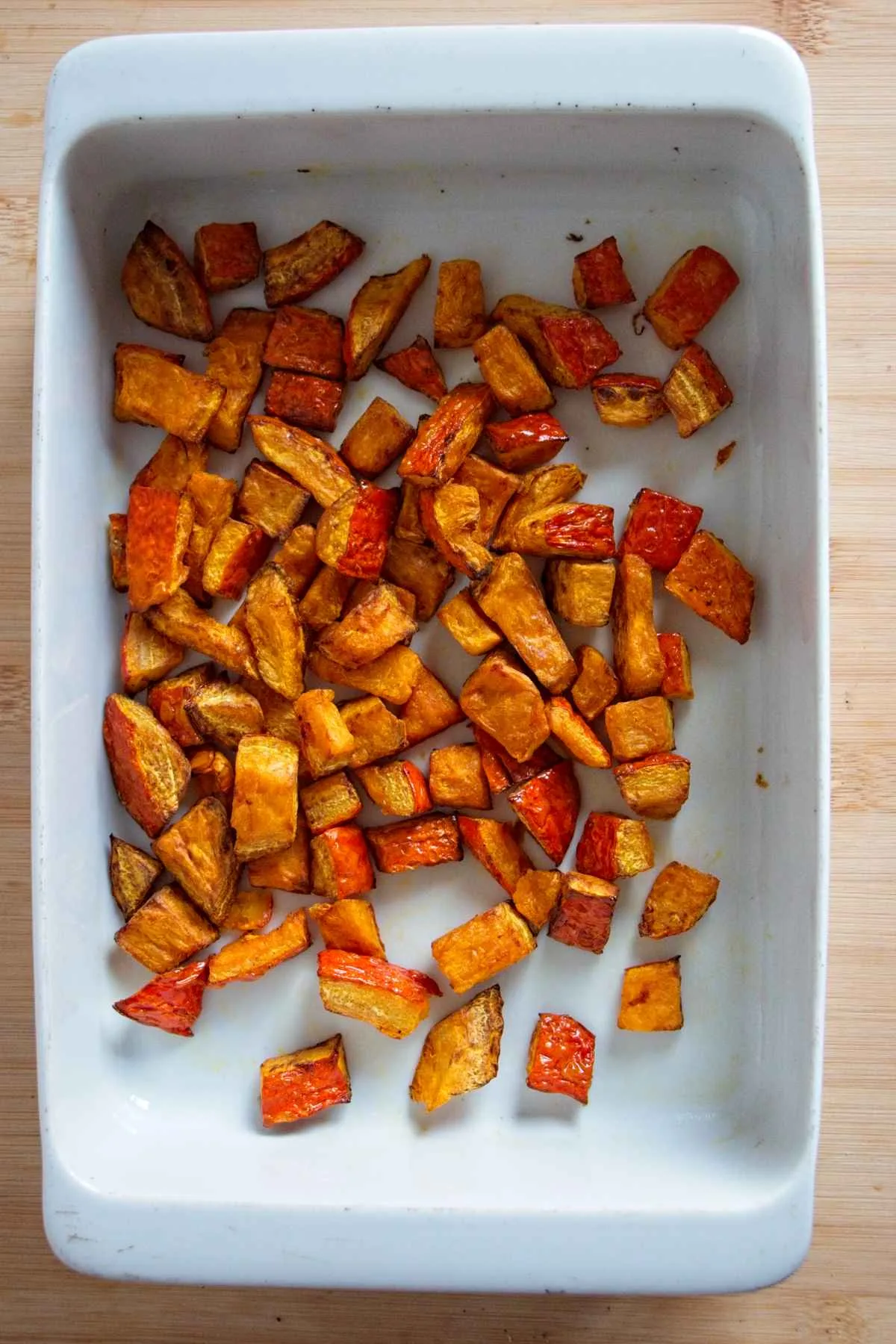 Caramelised roasted pumpkin pieces in a white baking dish after roasting.