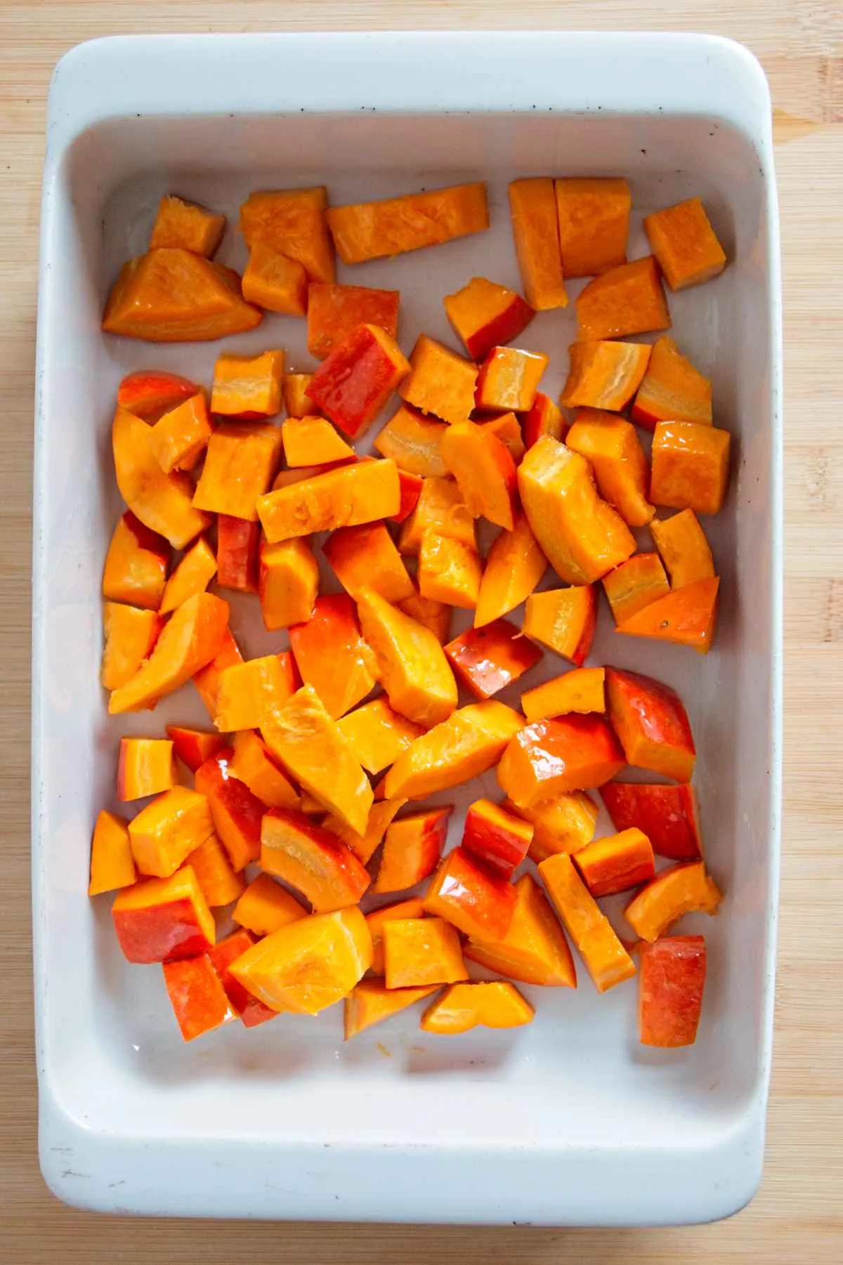Chunks of fresh pumpkin laid out in a white roasting dish, ready for the oven.