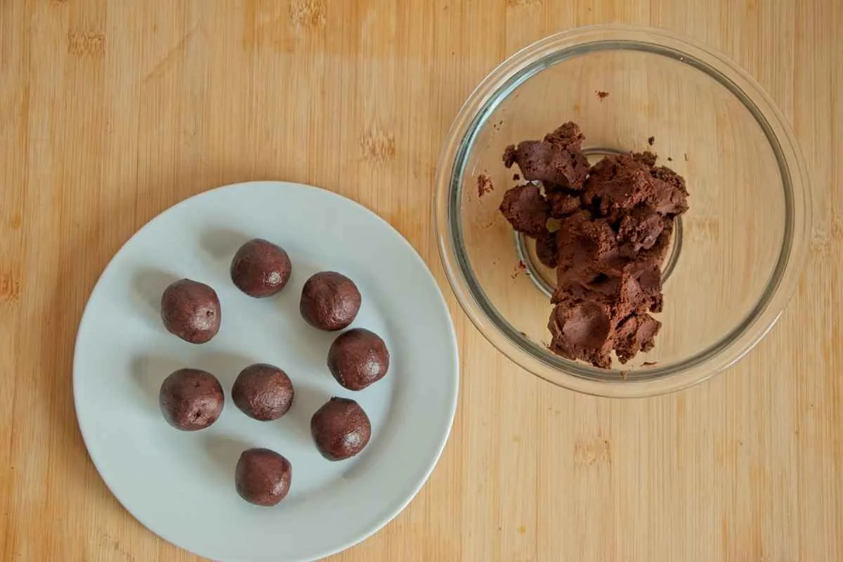 Rolled chocolate chestnut mixture on a plate with leftover mixture in a bowl on a wooden board.
