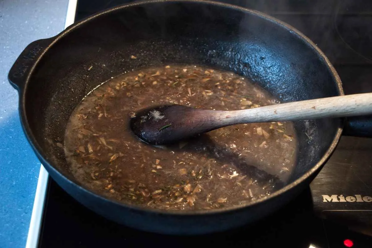 The vegan red wjne gravy simmering in a pan with chopped ceps and herbs.