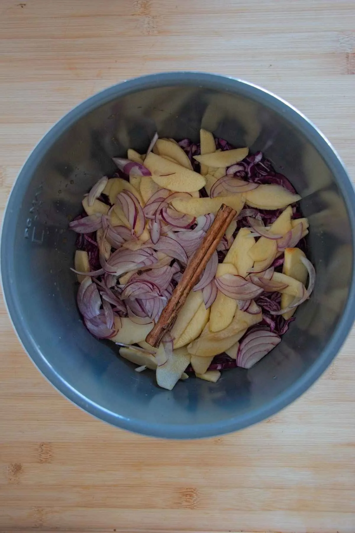 Layer of sliced apples, onions, and a cinnamon stick added on top of red cabbage in a slow cooker.