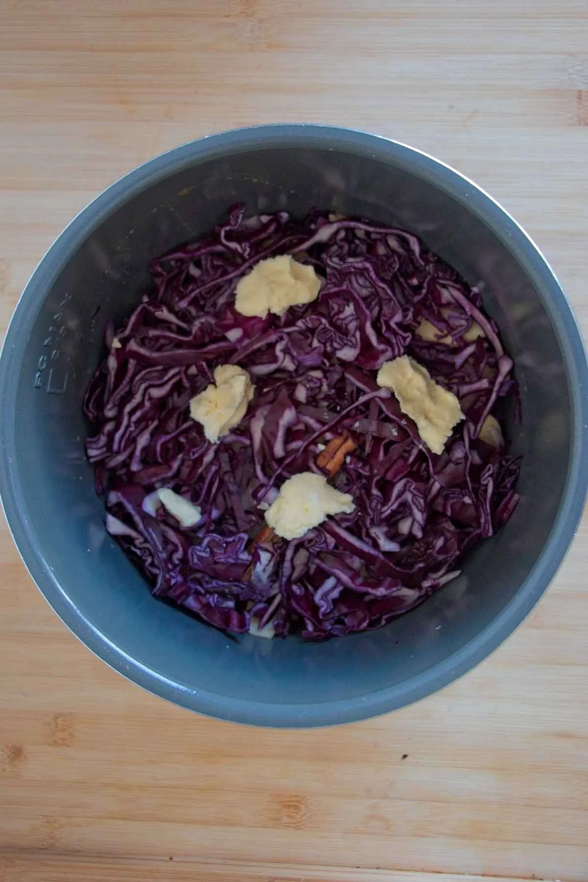 Shredded red cabbage in a slow cooker topped with small pieces of butter before cooking.