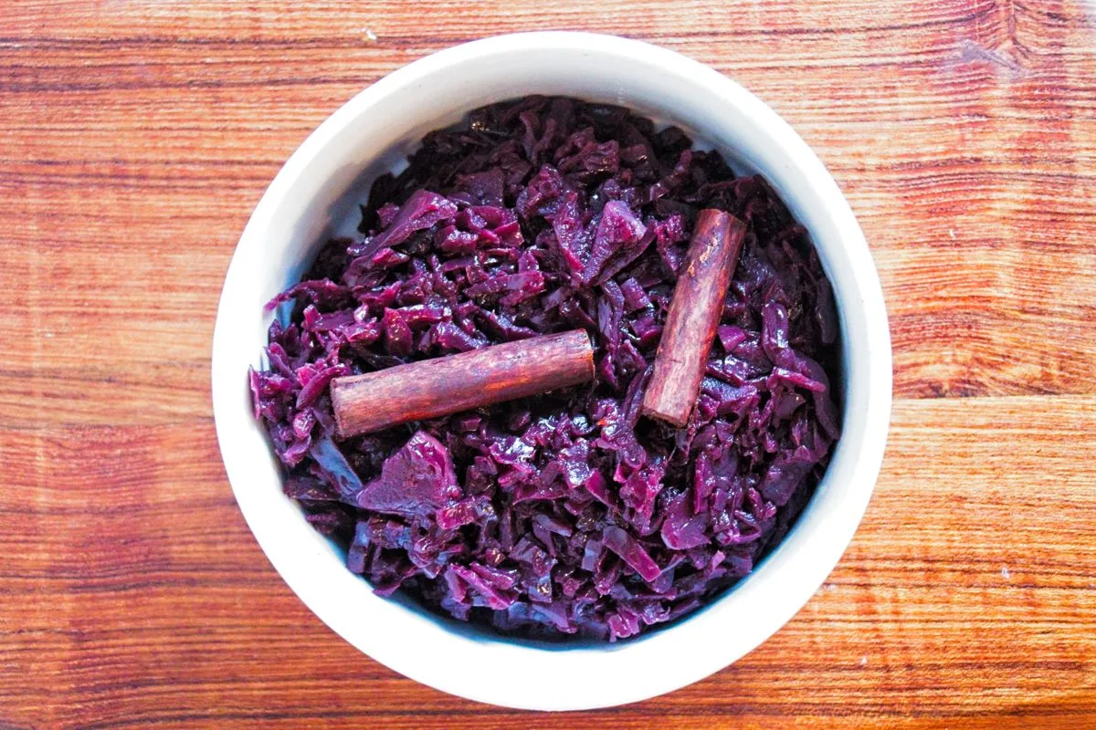 Slow-cooked red cabbage served in a white bowl with cinnamon sticks on top.