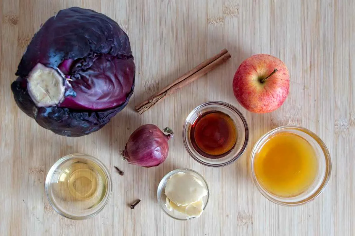 ngredients for slow-cooked red cabbage laid out on a wooden board, including red cabbage, apple, onion, spices, vinegar, and butter.