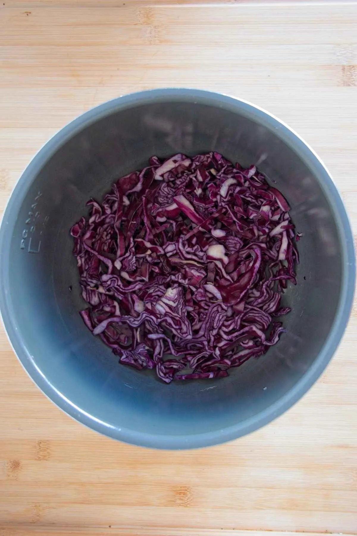 Shredded red cabbage placed in the base of a slow cooker before cooking.