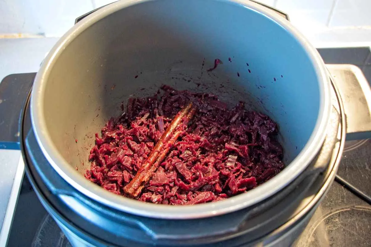Slow-cooked red cabbage simmering in a slow cooker with a cinnamon stick on top.