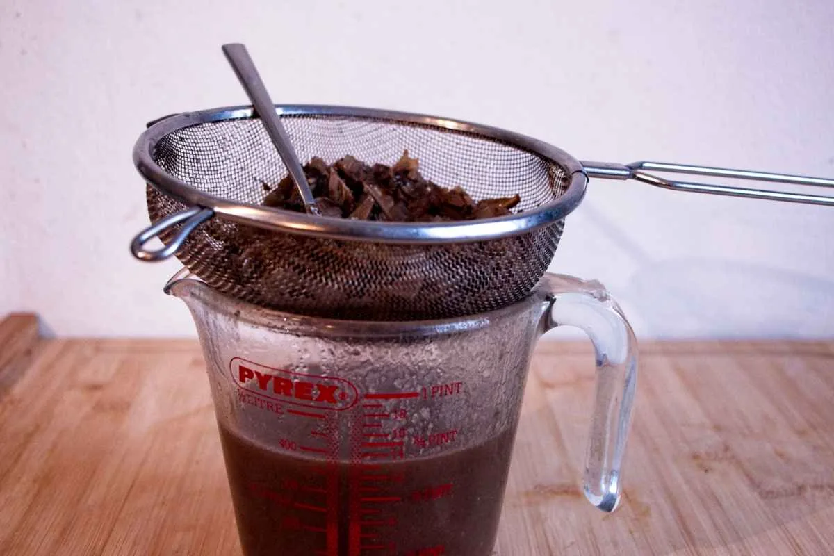 Straining cooked ceps and herbs over a jug of finished gravy.