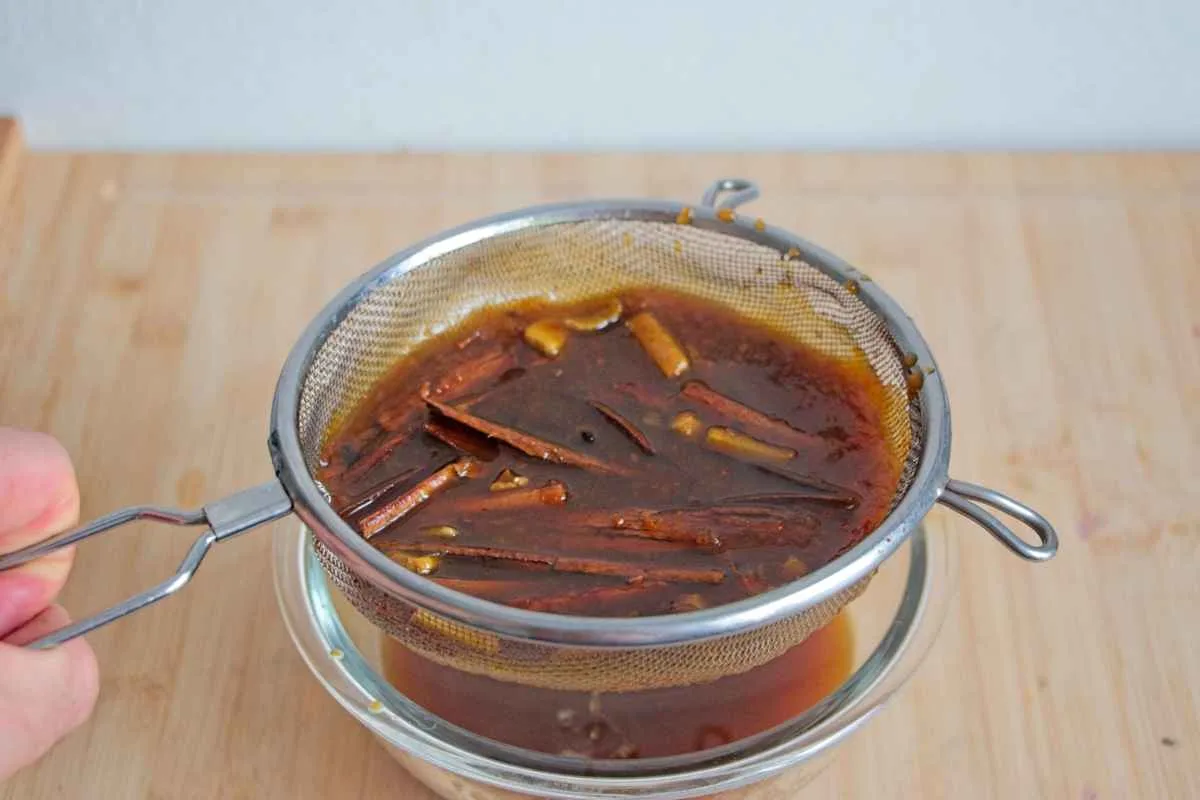 Warm spiced syrup being strained through a fine mesh sieve into a bowl.