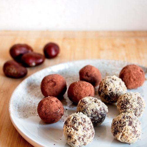 Vegan chestnut truffles on a light plate, coated in cocoa and crushed nuts.
