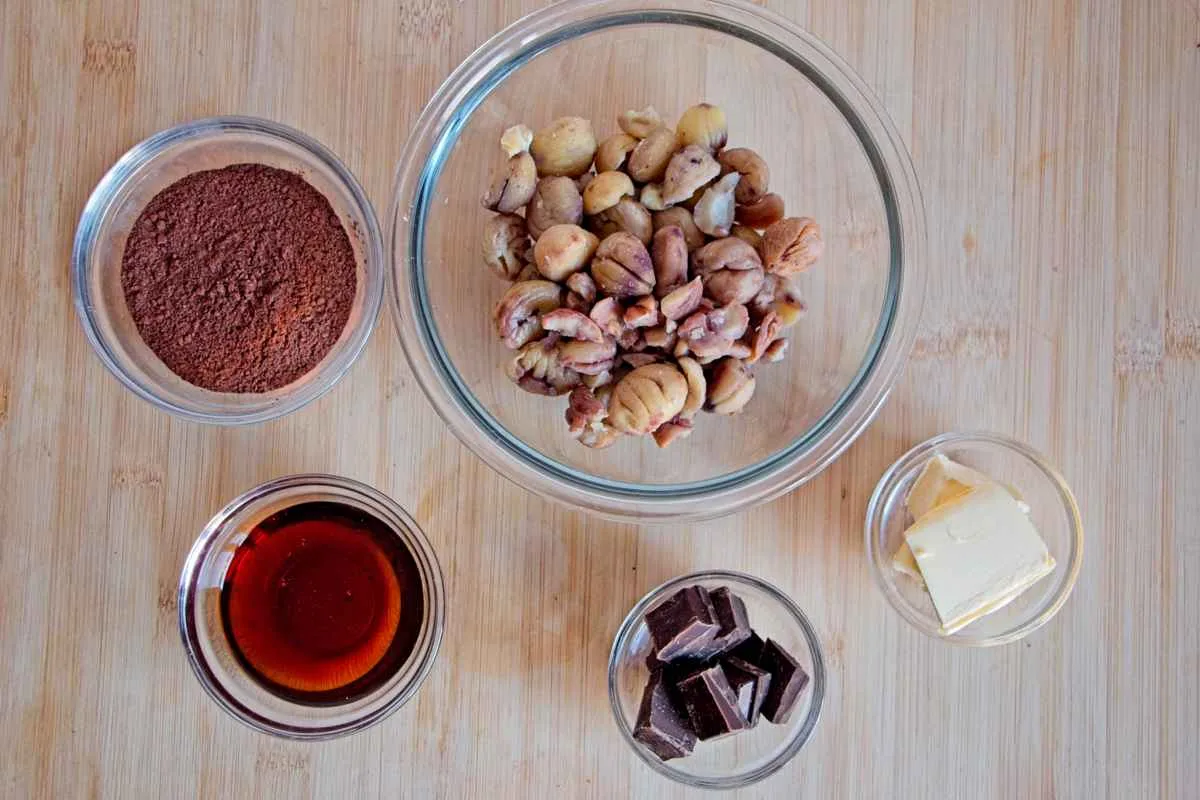 Ingredients for vegan chestnut truffles laid out in small bowls on a wooden board.