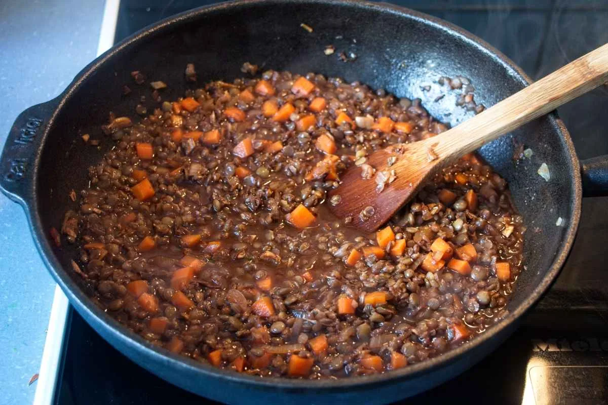 Vegetarian cottage pie with porcini filling simmering in a pan with a wooden spoon.