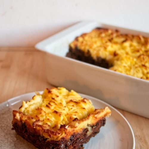 A served slice of vegetarian cottage pie with porcini on a plate, with the baked dish in the background.