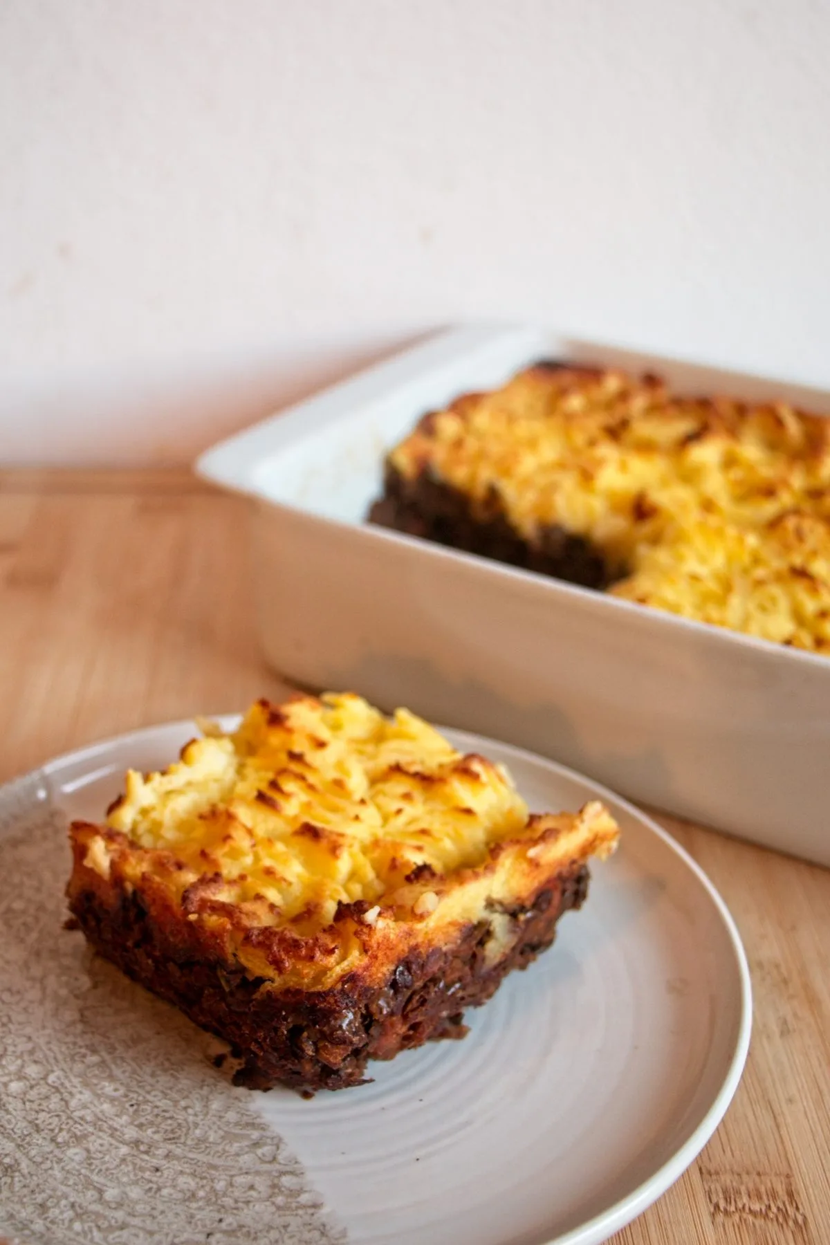 A served slice of vegetarian cottage pie with porcini on a plate, with the baked dish in the background.