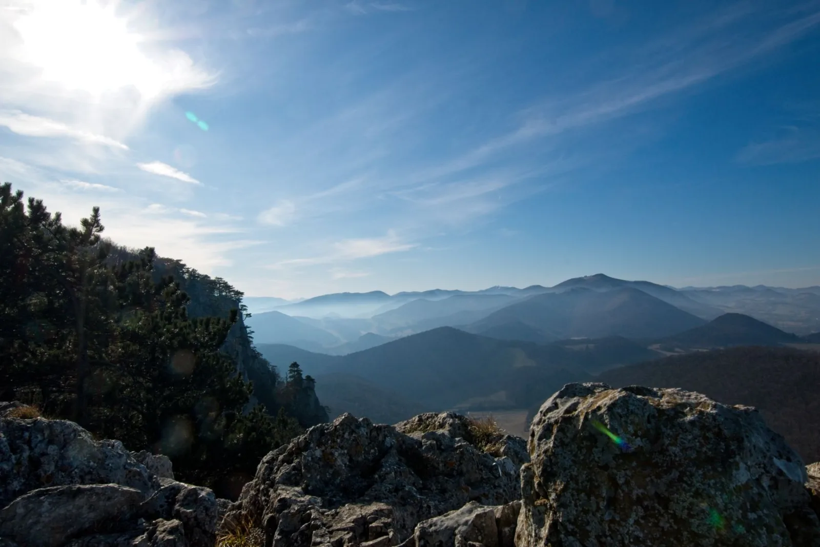 View over the Austrian mountains with misty layered peaks, rocky cliffs, and sunlight streaming across the sky.