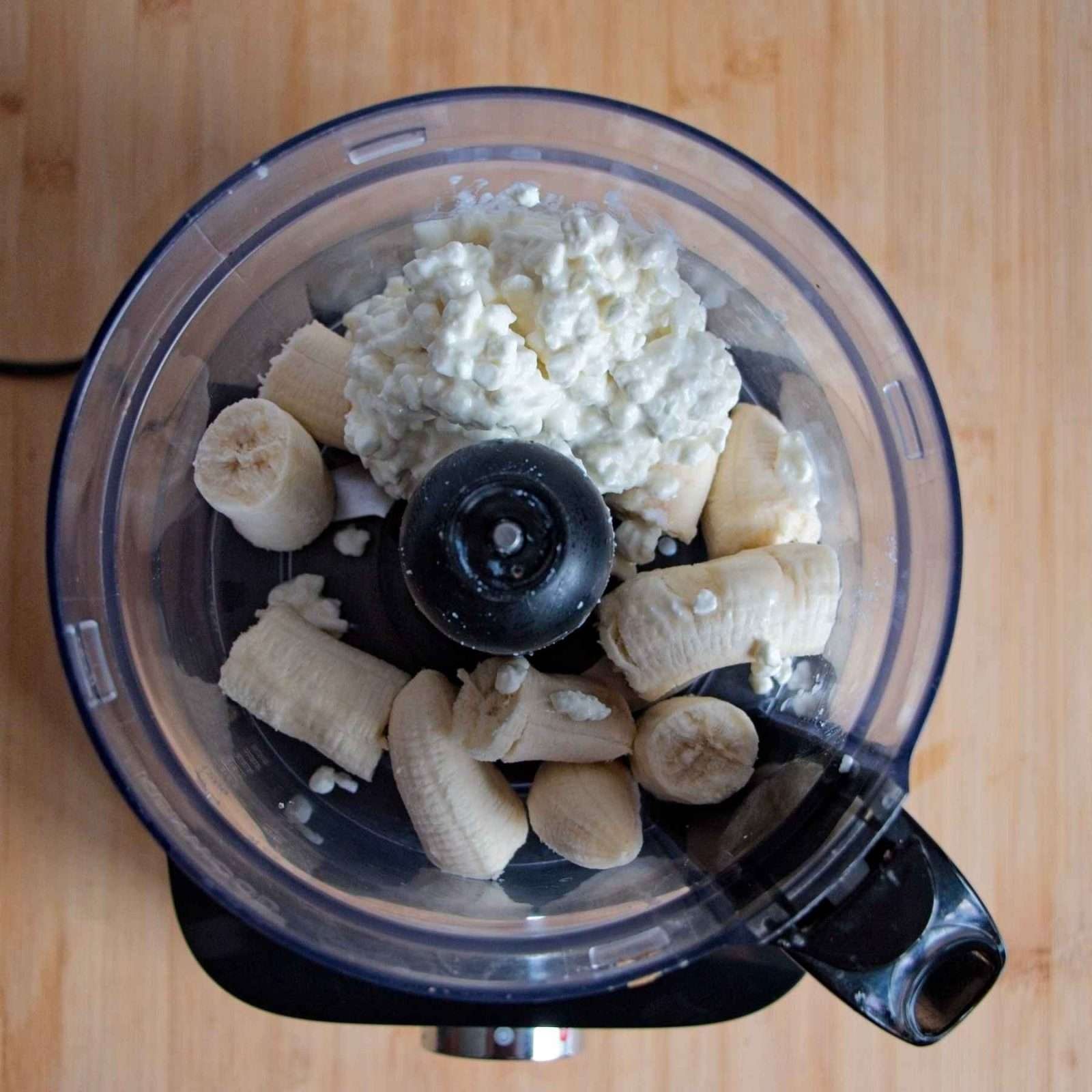 Food processor filled with sliced bananas and cottage cheese before blending.