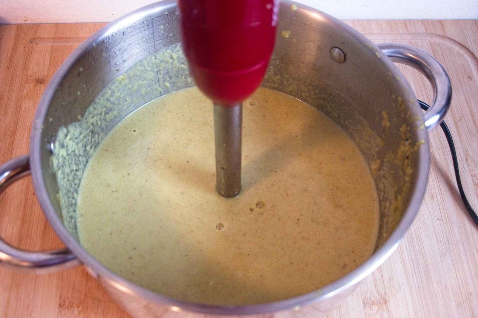 Curried cauliflower soup being blended in a pot with a hand blender until smooth.