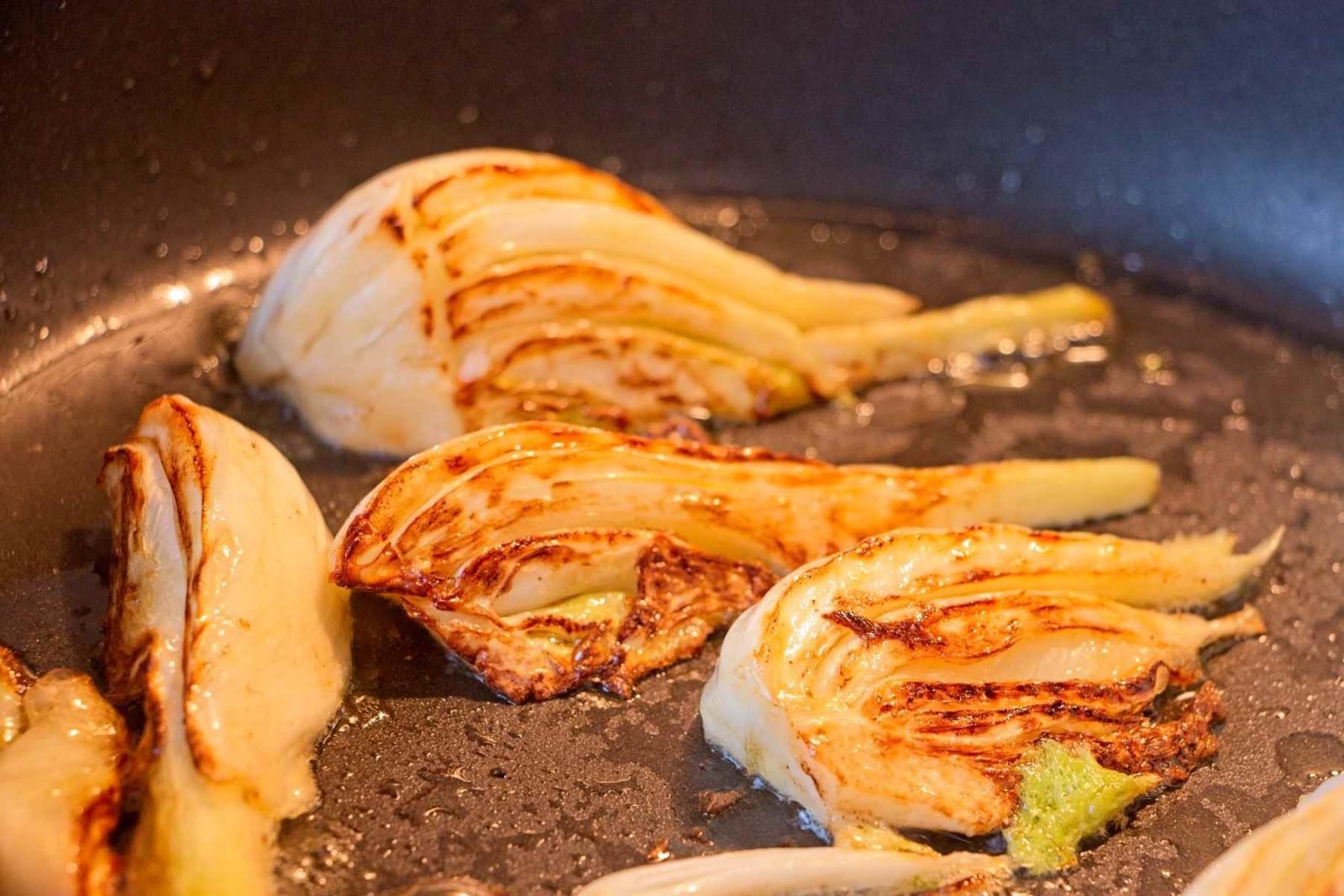 Fennel wedges caramelising cut-side down in a pan until golden brown.