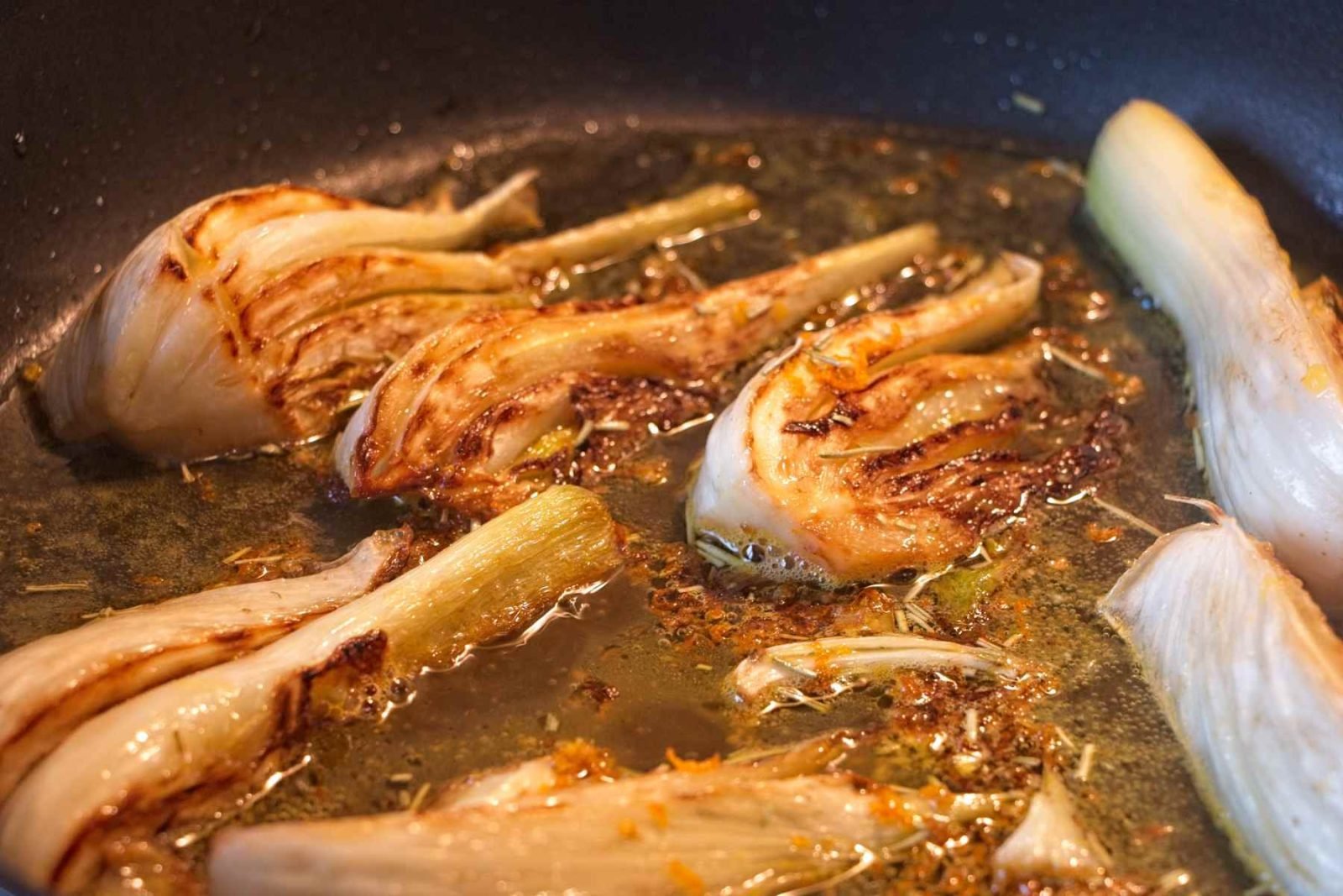 Caramelised fennel cooking in a pan with oil and aromatics, browning and reducing in the pan juices.