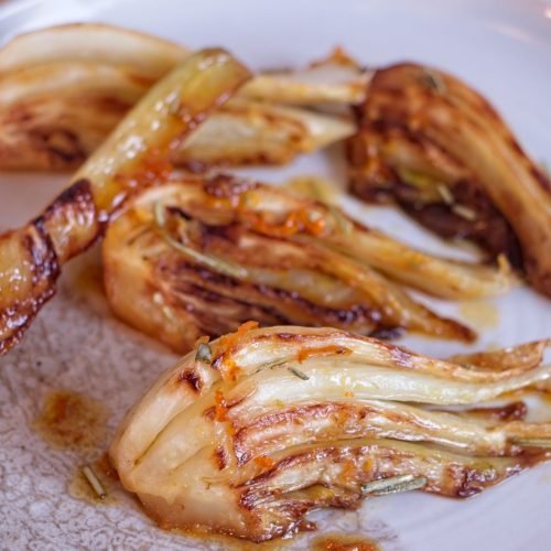Caramelised fennel wedges cooked until golden and lightly glazed, served on a white plate.