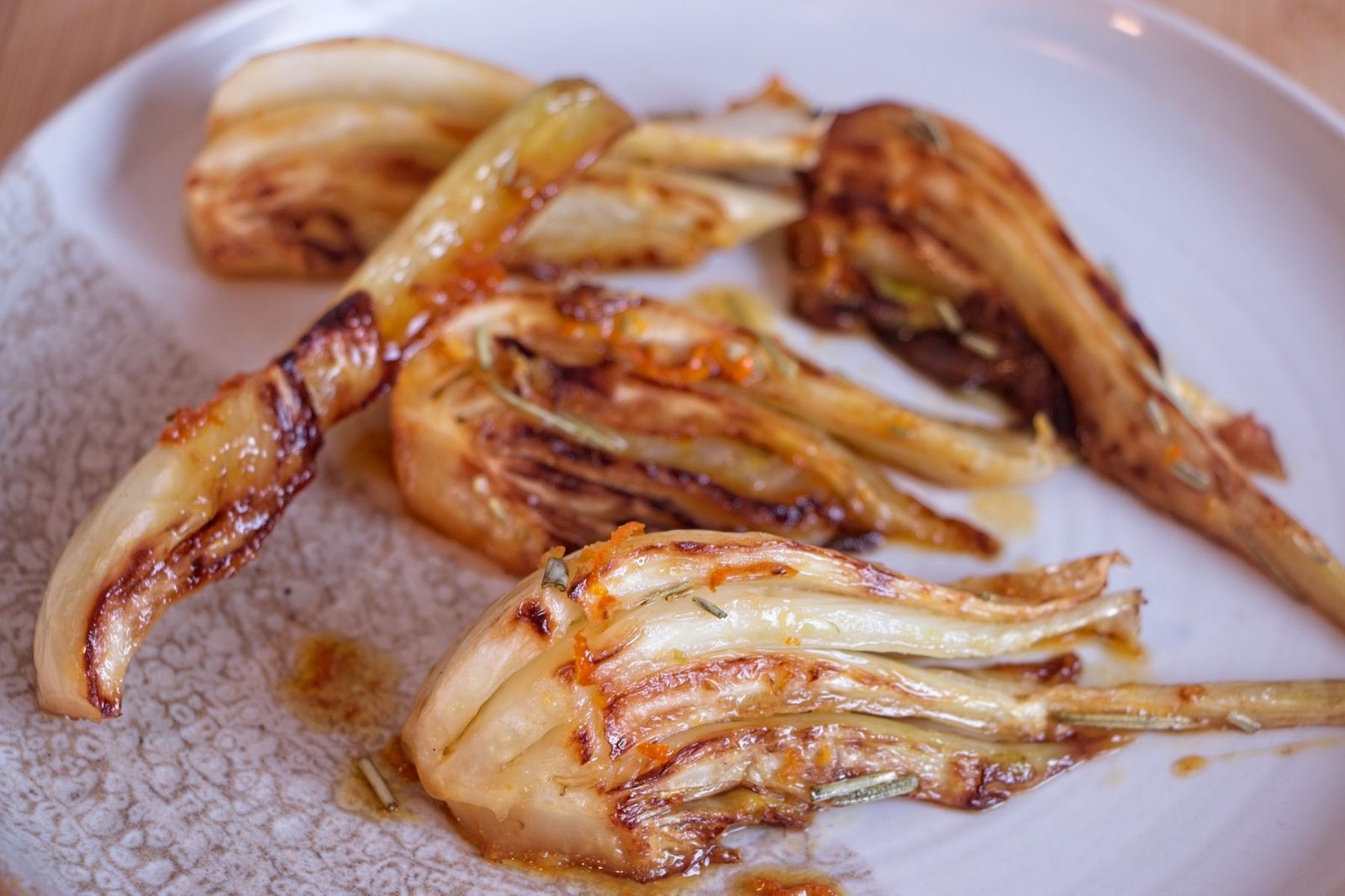 Caramelised fennel wedges cooked until golden and lightly glazed, served on a white plate.