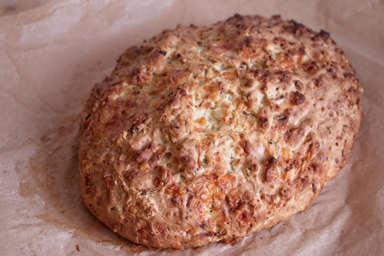 Close-up of cheddar onion soda bread with a deeply golden, scored crust just out of the oven.