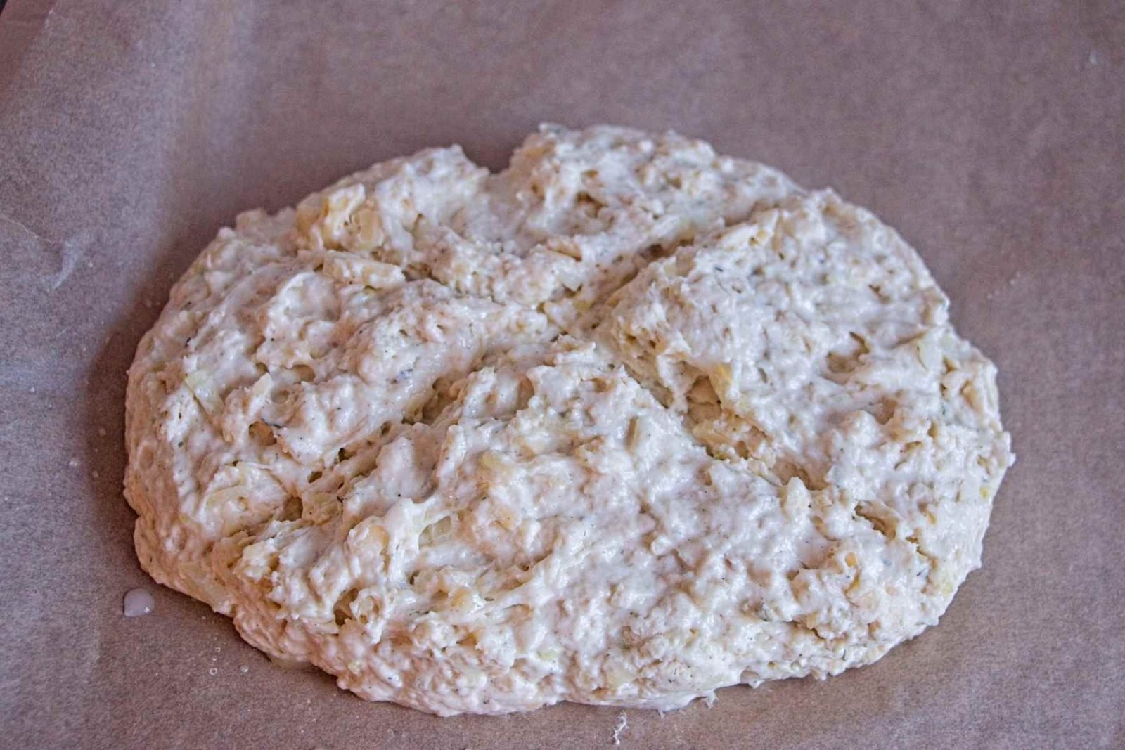 Unbaked cheddar onion soda bread dough shaped into a round loaf and scored before baking.