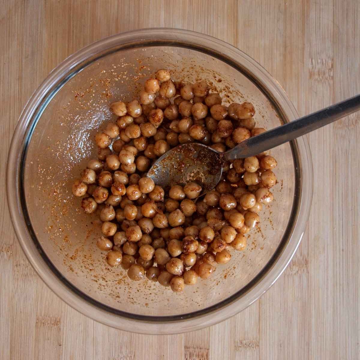 Chickpeas tossed with oil and spices in a glass bowl before roasting.