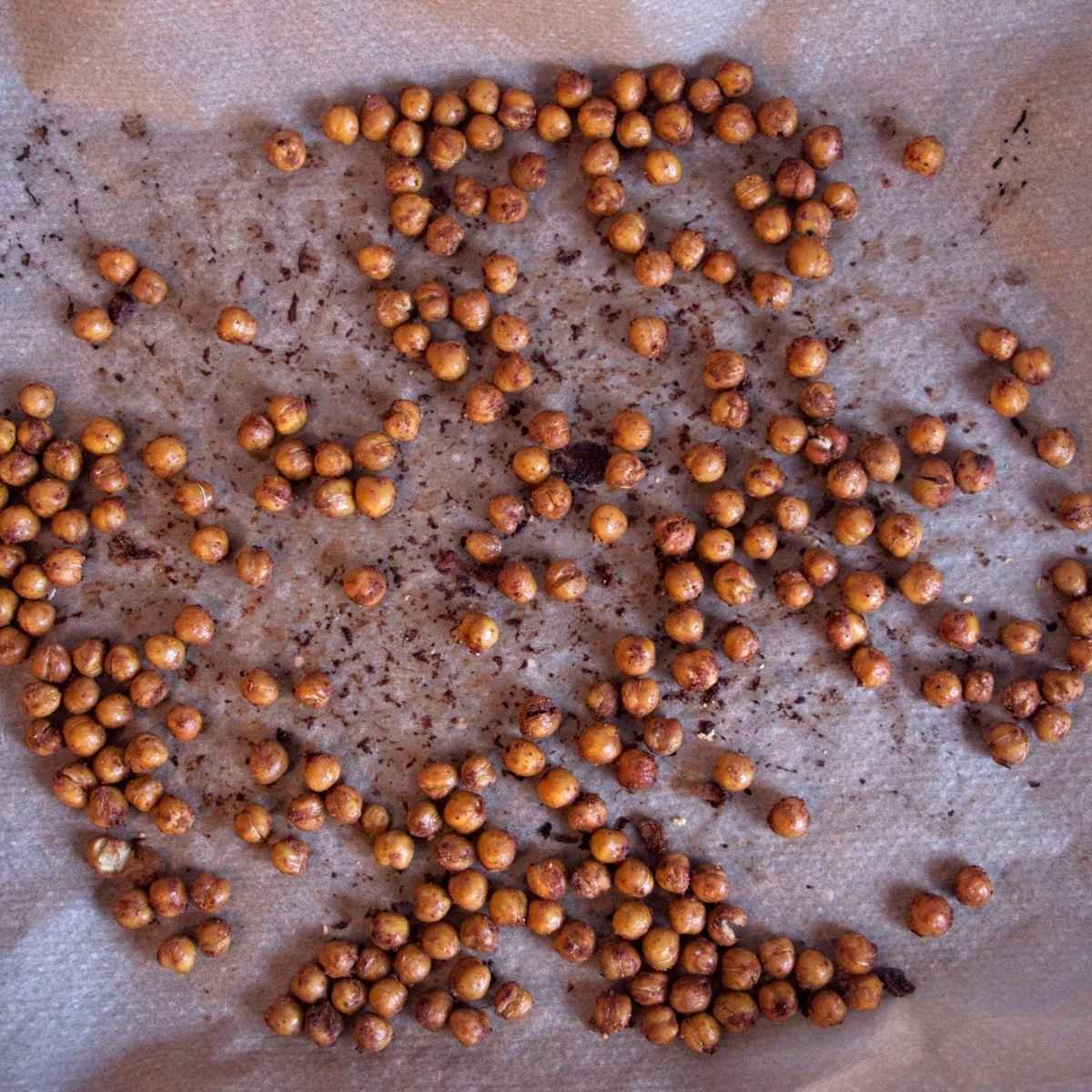 Roasted chickpeas spread across a parchment-lined baking tray after crisping in the oven.