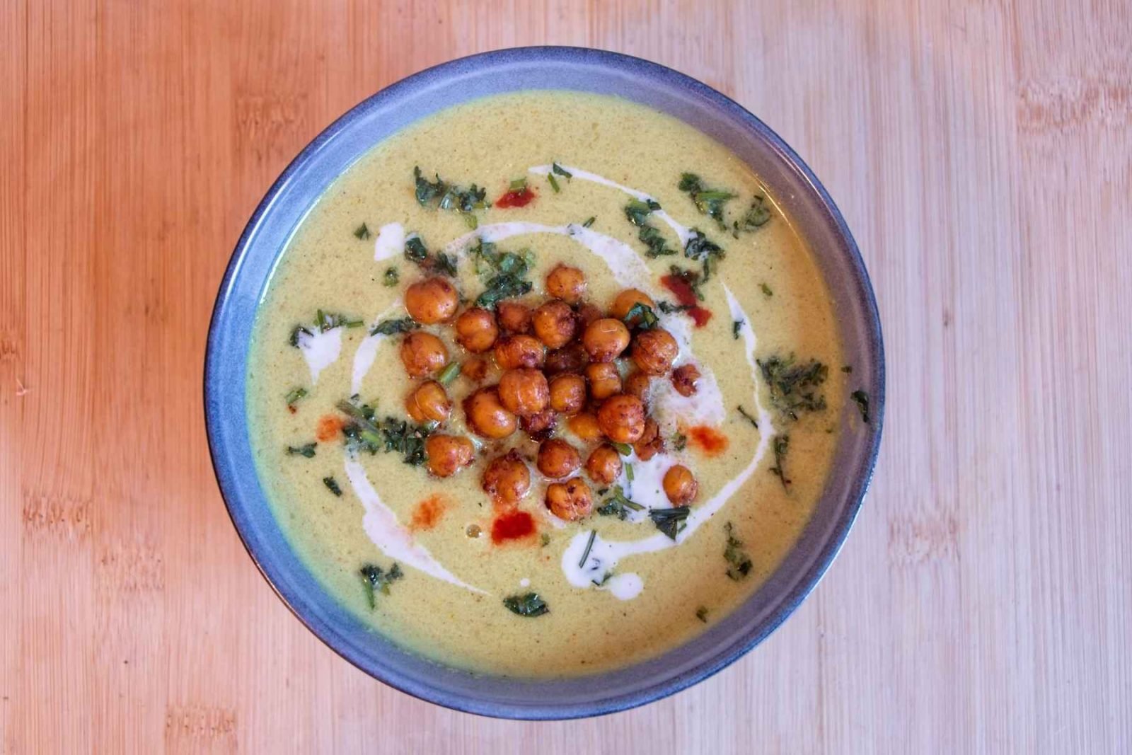 Curried cauliflower soup served in a bowl with coconut milk, crispy chickpeas, and herbs on top.
