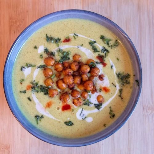 Curried cauliflower soup served in a bowl with coconut milk, crispy chickpeas, and herbs on top.