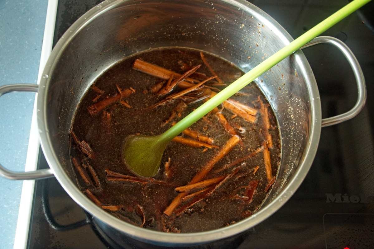 Gingerbread syrup simmering in a pot with cinnamon sticks and cloves, stirred with a green spoon.