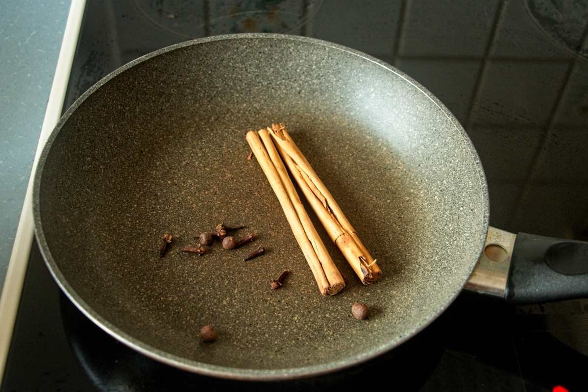 Whole cinnamon sticks, cloves, and allspice berries toasting in a dry pan to release their aroma.