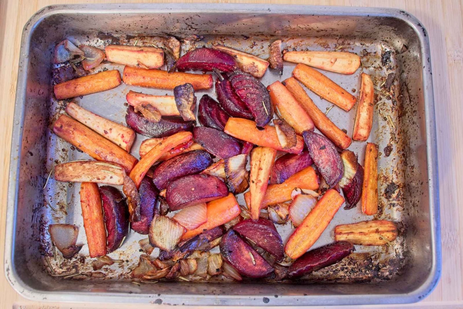 Honey mustard roasted root vegetables on an oven tray, with carrots, parsnips, beetroot, and caramelised onions