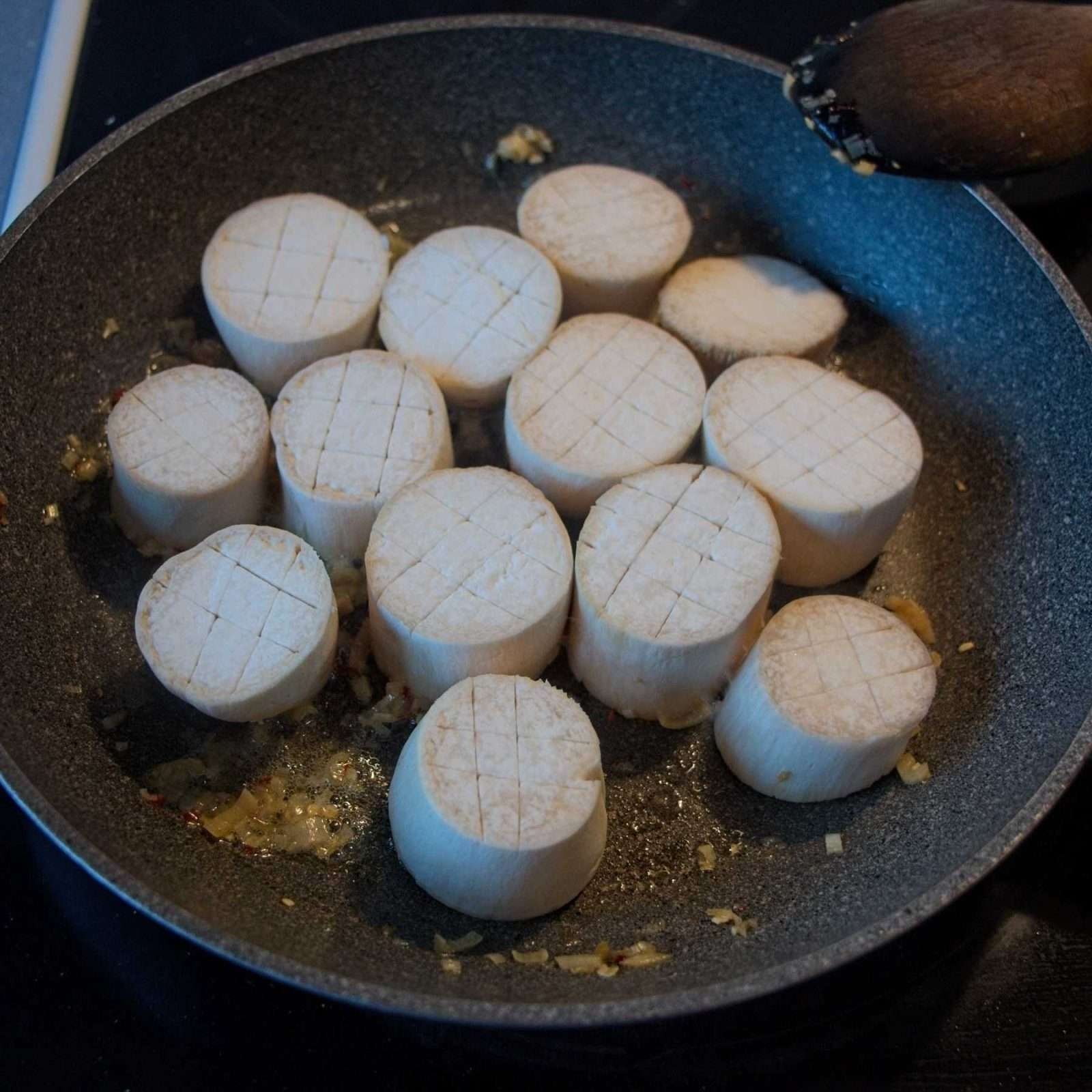 Raw mushroom rounds with crosshatch scoring arranged in a pan with chopped garlic, ready to be seared.