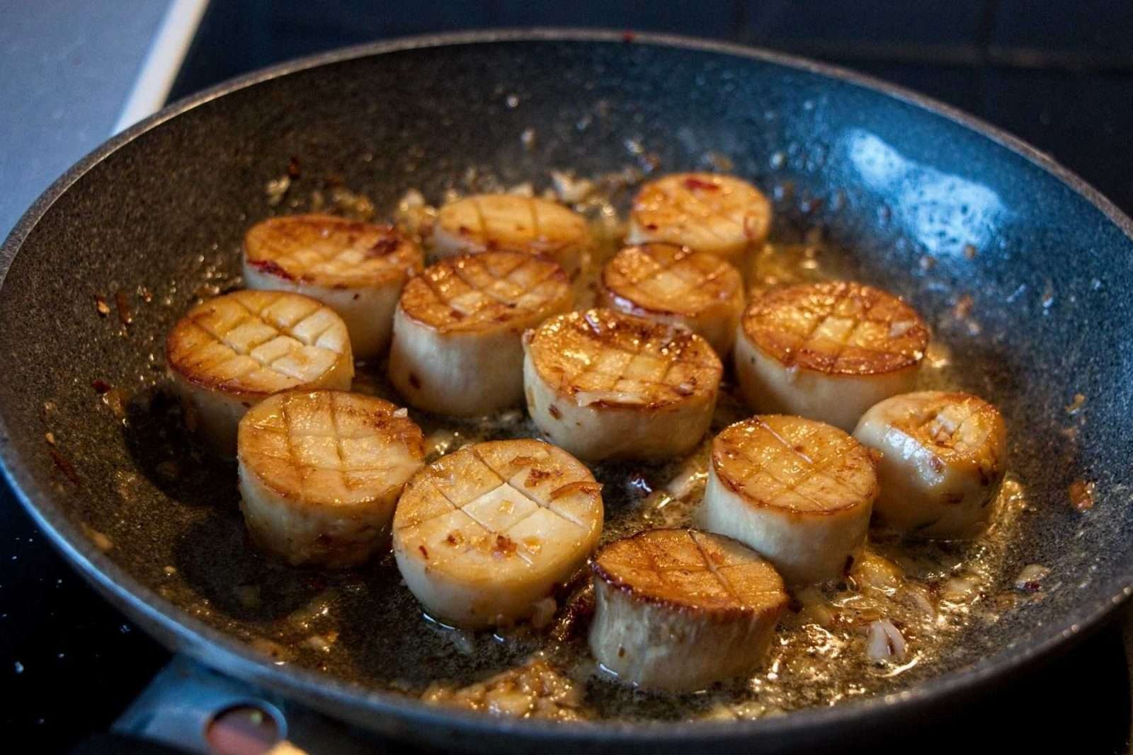 King oyster mushroom scallops browning in a pan with garlic, lemongrass, and butter midway through cooking.