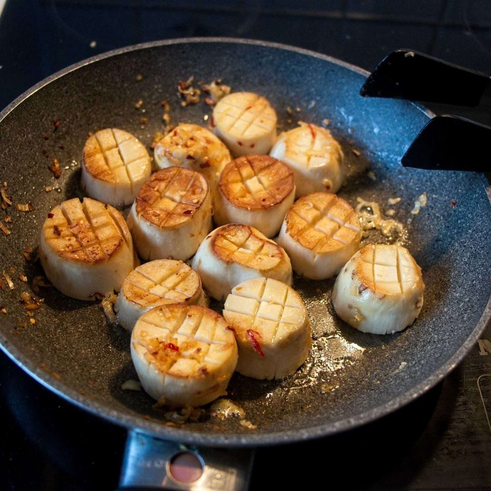 Pan of golden seared mushroom rounds with garlic, chilli, and lemongrass in melted butter.
