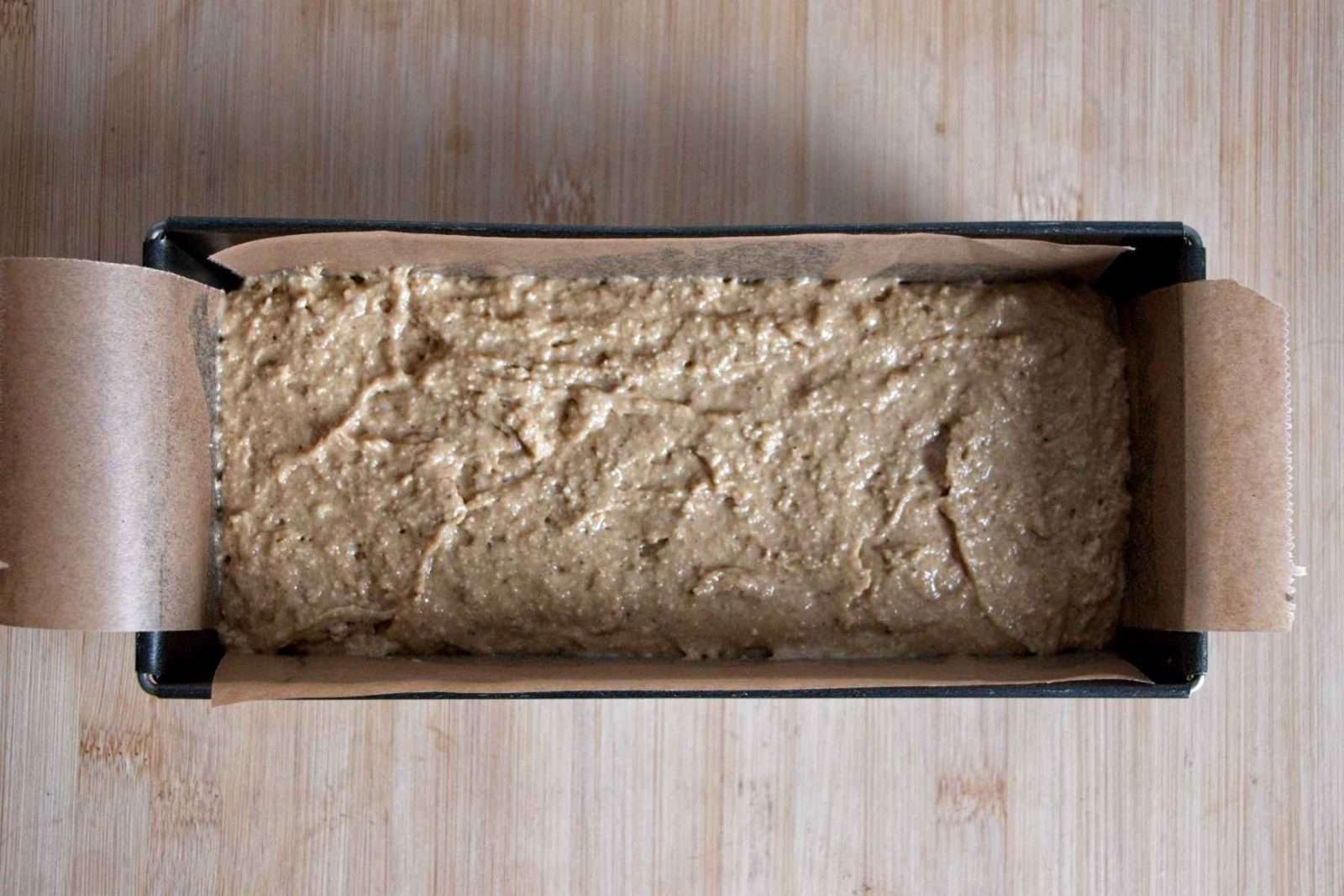 Loaf tin lined with parchment and filled with banana bread batter ready for baking.