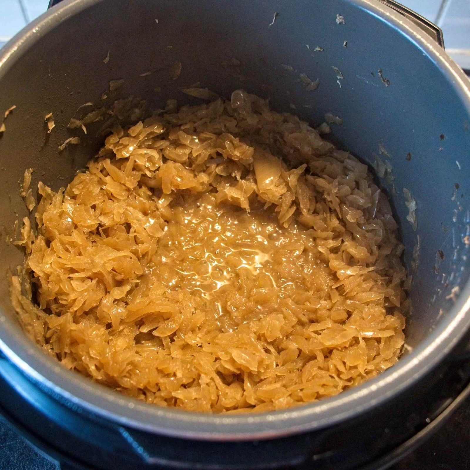 Softened onions after ten hours cooking, pale golden and sitting in their released liquid before the final browning stage.
