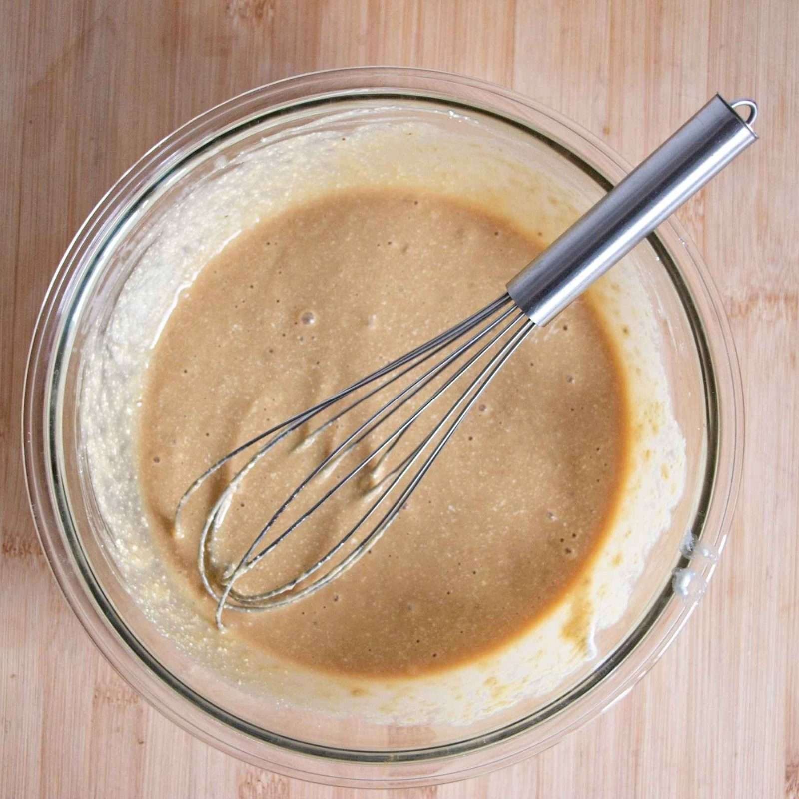A bowl of batter being whisked on a wooden surface.