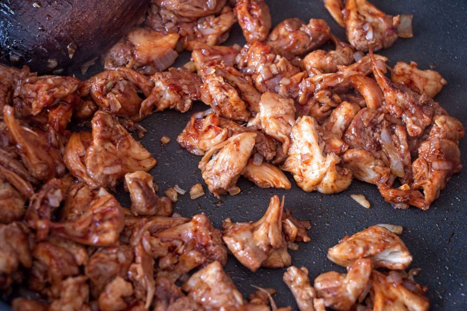 Shredded lion’s mane mushrooms cooking in a pan with BBQ sauce until sticky and browned