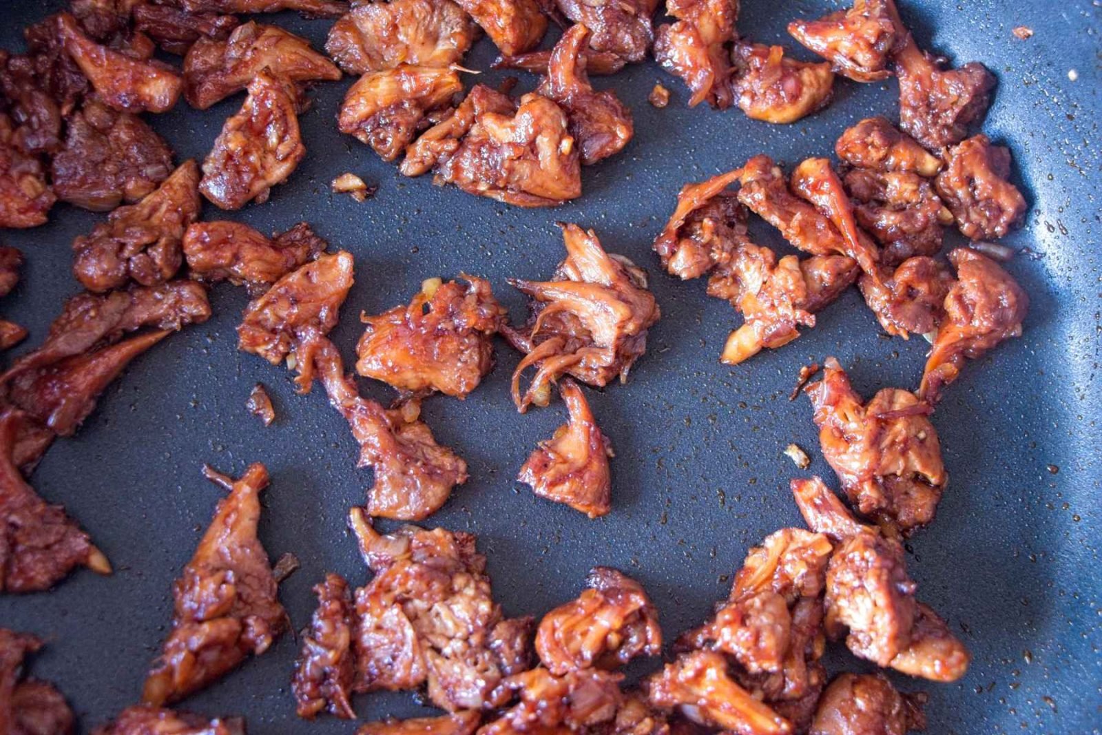 Crispy mushroom pieces cooking in a pan as the sauce thickens and caramelises