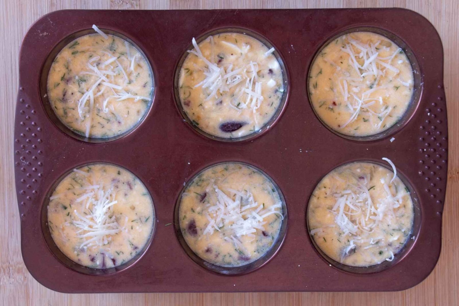 Muffin tin filled with cottage cheese batter and topped with grated cheese before baking