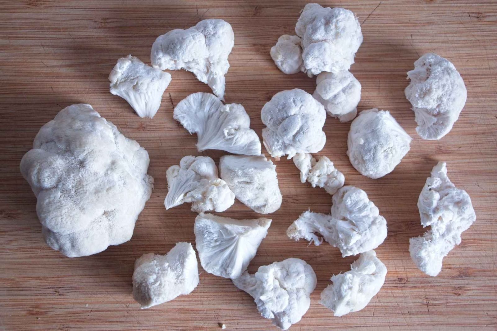 Fresh lion’s mane mushrooms torn into pieces on a wooden chopping board