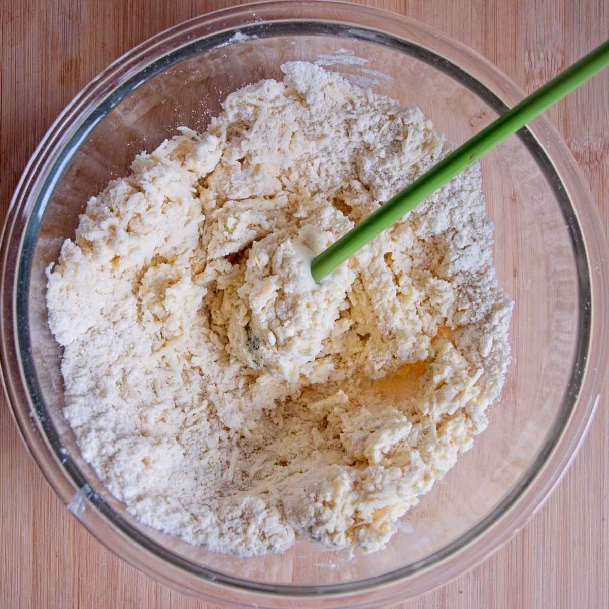Scone dough being mixed in a glass bowl with a spatula as the wet ingredients are combined